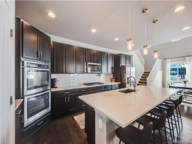 kitchen featuring pendant lighting, sink, stainless steel appliances, and a center island with sink