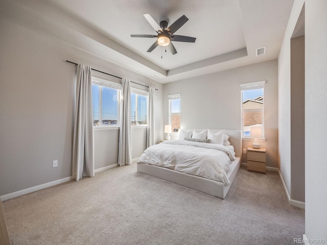 bedroom featuring a raised ceiling, light carpet, and multiple windows