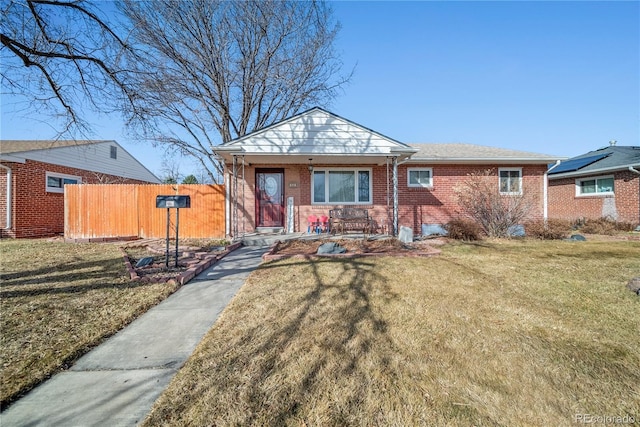 view of front facade featuring a porch, a front yard, brick siding, and fence