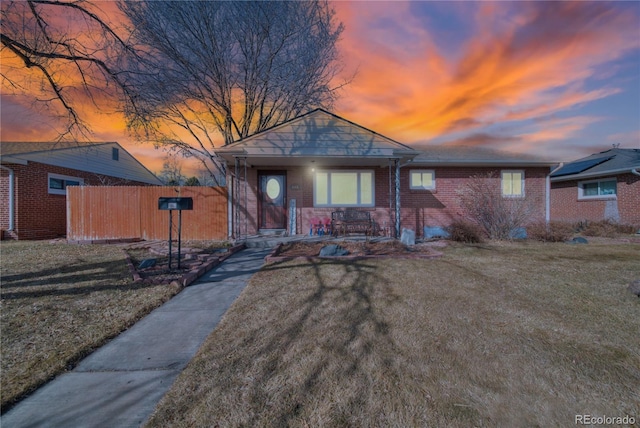 bungalow-style home with a porch, brick siding, a yard, and fence