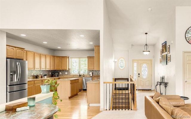 kitchen featuring sink, stainless steel appliances, a kitchen island, light brown cabinetry, and decorative light fixtures