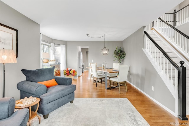 living area featuring a chandelier, wood finished floors, baseboards, and stairs