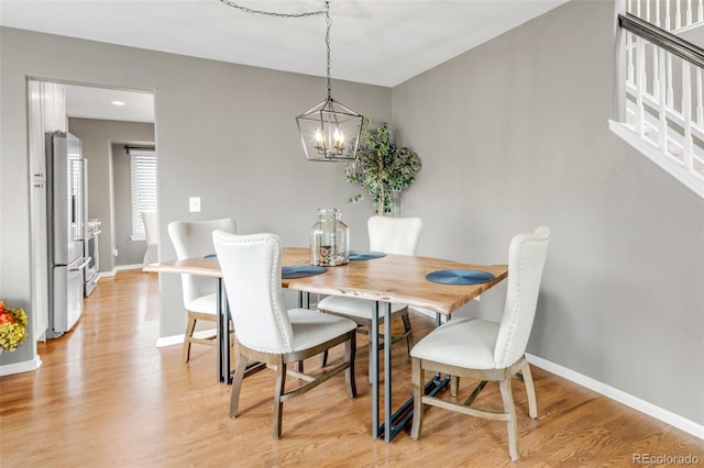 dining space featuring light wood-style flooring, baseboards, and a notable chandelier