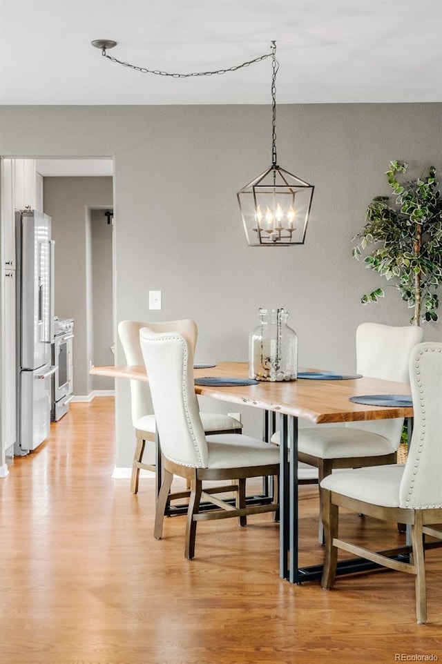 dining area with a chandelier, baseboards, and light wood finished floors