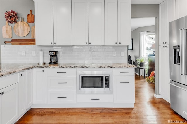 kitchen with stainless steel appliances, white cabinetry, backsplash, light stone countertops, and light wood finished floors