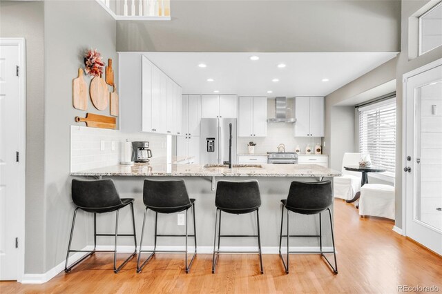 kitchen with light wood finished floors, white cabinets, wall chimney exhaust hood, a peninsula, and stainless steel appliances