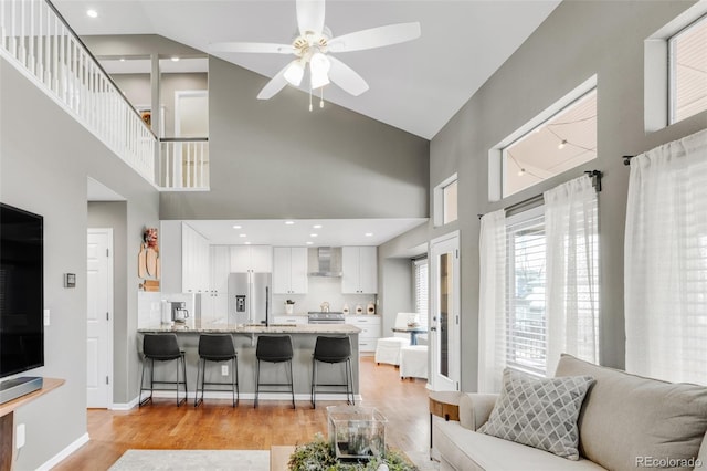 living area with recessed lighting, light wood-style flooring, a ceiling fan, high vaulted ceiling, and baseboards