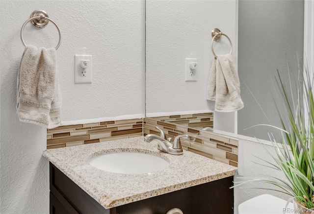 half bathroom featuring a textured wall, toilet, vanity, and decorative backsplash