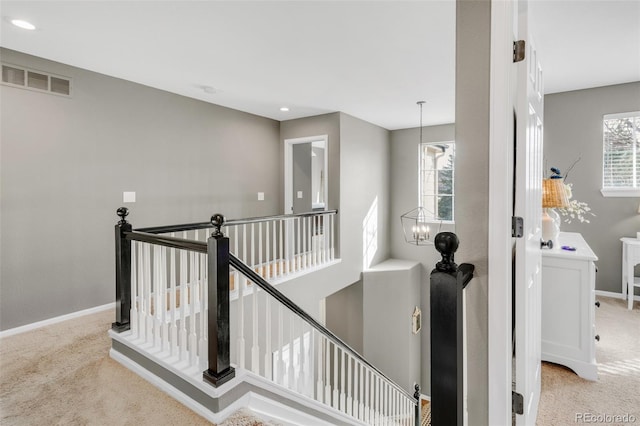 hall featuring carpet, visible vents, a notable chandelier, and an upstairs landing