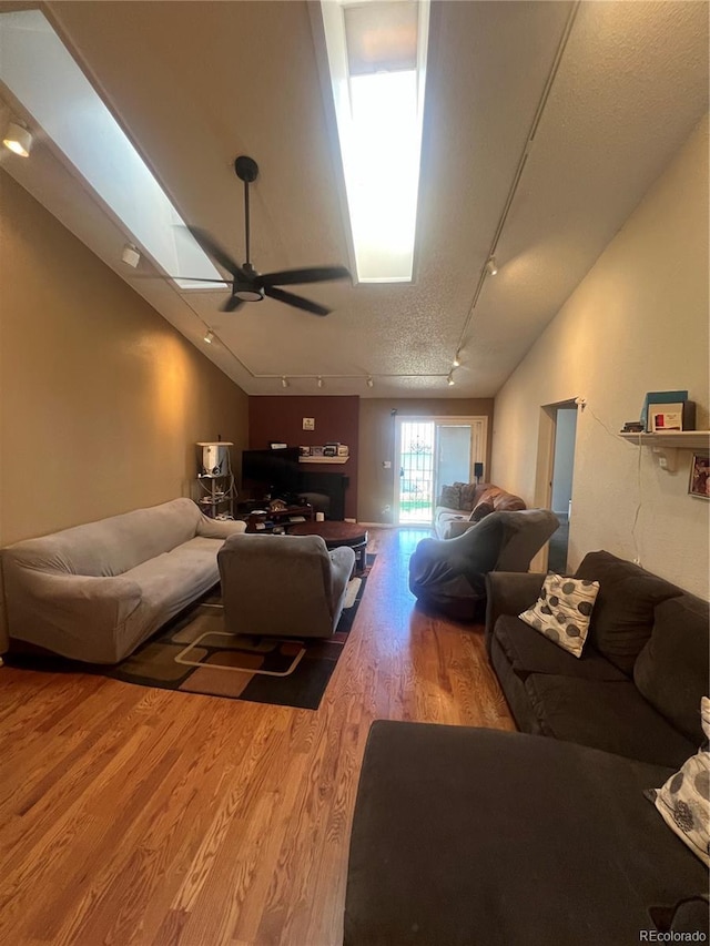 living area featuring rail lighting, wood finished floors, a ceiling fan, a textured ceiling, and lofted ceiling