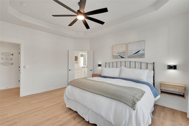 bedroom featuring a tray ceiling, ensuite bath, ceiling fan, and hardwood / wood-style flooring