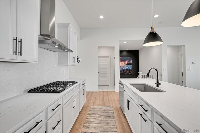 kitchen featuring appliances with stainless steel finishes, pendant lighting, white cabinetry, sink, and wall chimney exhaust hood