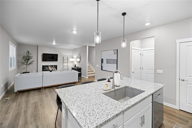 kitchen with dishwasher, a center island with sink, sink, hanging light fixtures, and white cabinetry