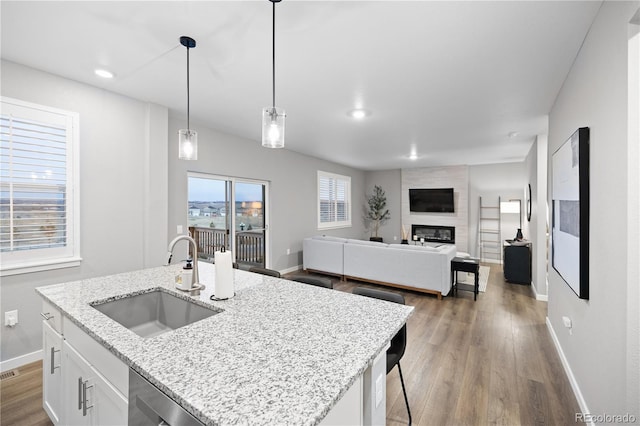 kitchen with white cabinets, a center island with sink, sink, decorative light fixtures, and a large fireplace