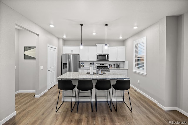 kitchen with hardwood / wood-style floors, a kitchen island with sink, appliances with stainless steel finishes, light stone counters, and white cabinetry