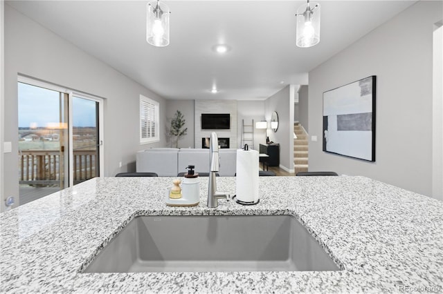 kitchen featuring decorative light fixtures, a large fireplace, light stone countertops, and sink