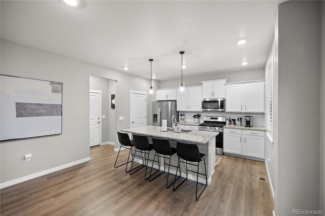 kitchen featuring white cabinetry, light stone counters, decorative light fixtures, a center island with sink, and appliances with stainless steel finishes