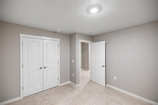 unfurnished bedroom featuring light colored carpet, a textured ceiling, and a closet