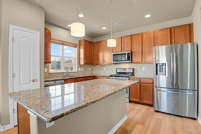 kitchen featuring sink, hanging light fixtures, stainless steel appliances, light hardwood / wood-style floors, and a kitchen island