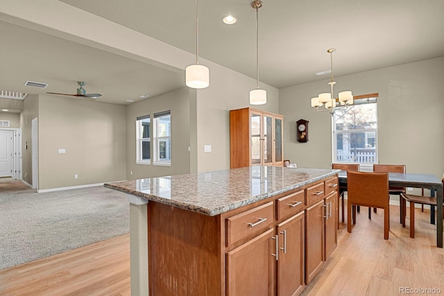 kitchen featuring ceiling fan with notable chandelier, a kitchen island, decorative light fixtures, and light wood-type flooring