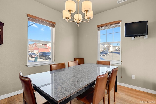 dining space with a wealth of natural light, light hardwood / wood-style floors, and an inviting chandelier