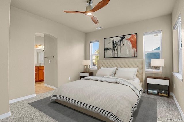 bedroom with ceiling fan, light carpet, and connected bathroom