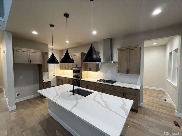 kitchen featuring light stone countertops, decorative light fixtures, a kitchen island with sink, and sink