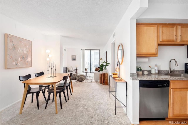 kitchen with light brown cabinets, a sink, a textured ceiling, stainless steel dishwasher, and light colored carpet