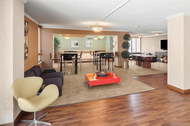 living room with a textured ceiling, wood finished floors, baseboards, and ornamental molding