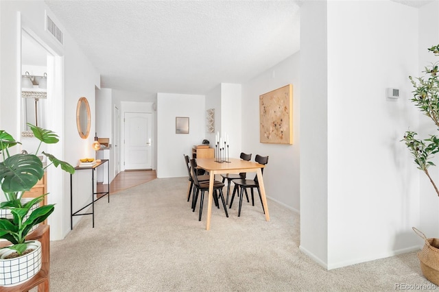 carpeted dining space featuring visible vents, a textured ceiling, and baseboards