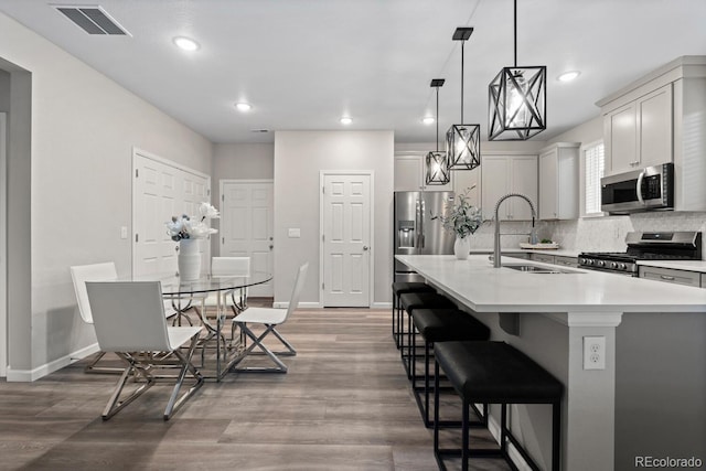 kitchen featuring stainless steel appliances, a sink, wood finished floors, decorative backsplash, and baseboards