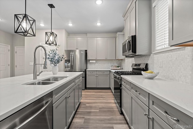 kitchen featuring appliances with stainless steel finishes, a sink, gray cabinets, pendant lighting, and light wood-style flooring