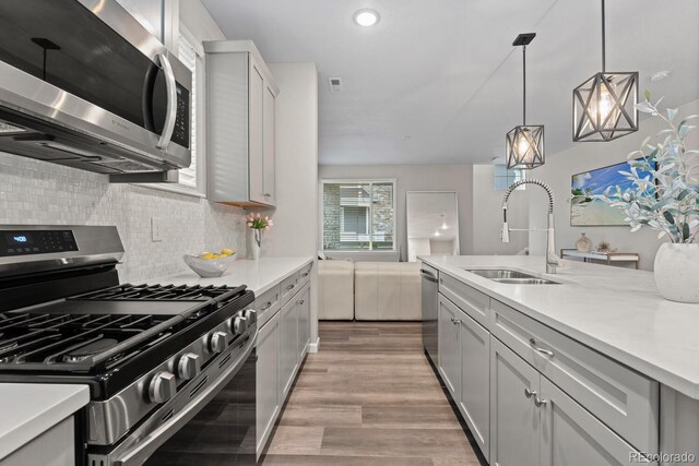 kitchen with stainless steel appliances, a sink, light countertops, light wood finished floors, and recessed lighting