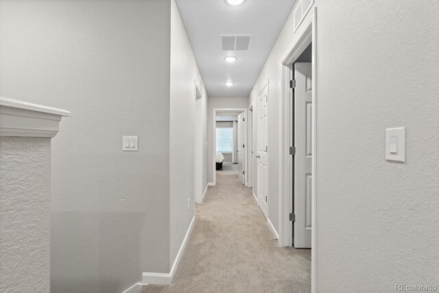 hall with light colored carpet, baseboards, and a textured wall