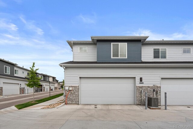 view of front of property with stone siding, a garage, driveway, and central AC unit