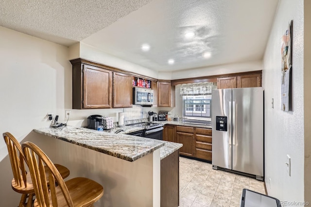 2072 S Helena St Unit B, Aurora, CO 80013 - kitchen featuring appliances with stainless steel finishes, a peninsula, a textured ceiling, a kitchen breakfast bar, and light stone countertops