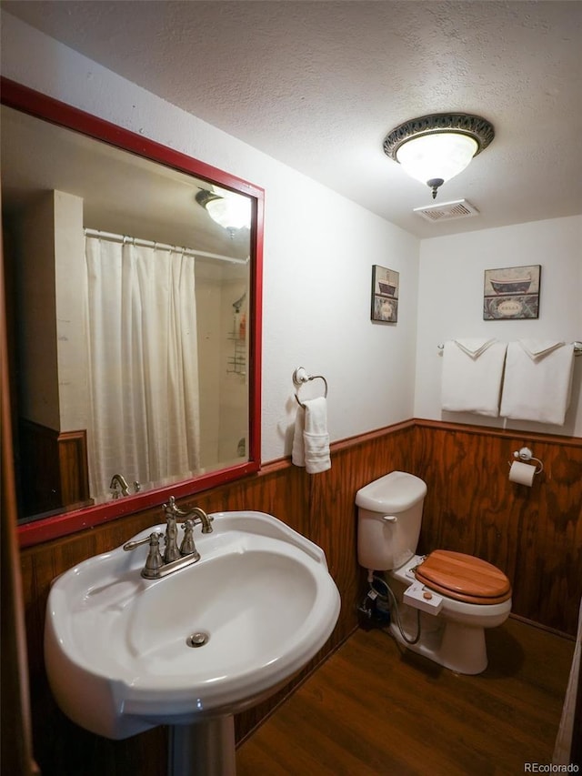 full bath with a wainscoted wall, toilet, a textured ceiling, wooden walls, and wood finished floors