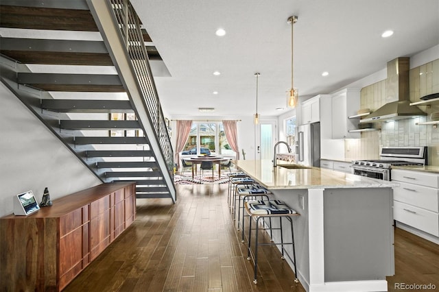 kitchen featuring decorative light fixtures, white cabinets, a large island, stainless steel appliances, and wall chimney exhaust hood