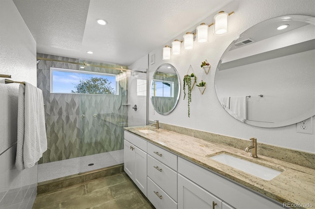 bathroom featuring tiled shower, vanity, and a textured ceiling