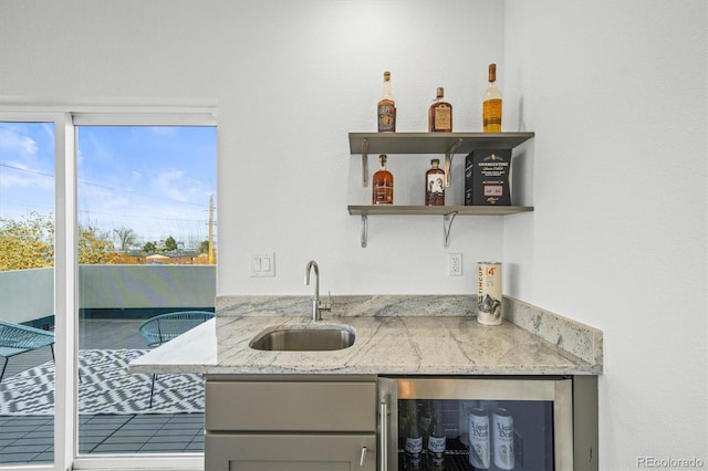 bar featuring wine cooler, sink, light stone countertops, and gray cabinetry