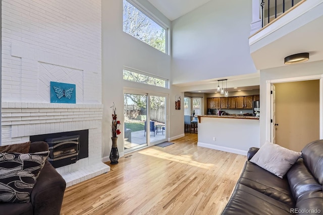 living room with a fireplace, a high ceiling, baseboards, and light wood-type flooring