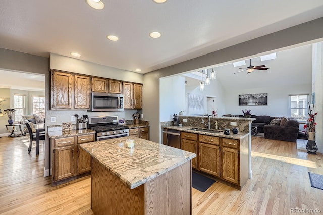 kitchen featuring a sink, a peninsula, brown cabinetry, appliances with stainless steel finishes, and open floor plan