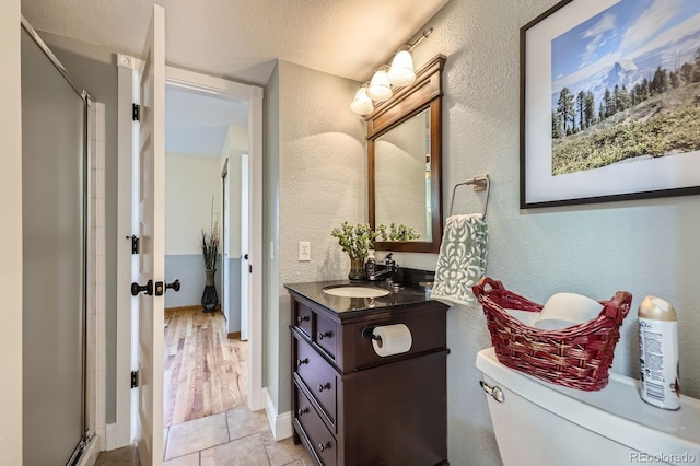 full bathroom with a shower stall, a textured wall, toilet, vanity, and baseboards
