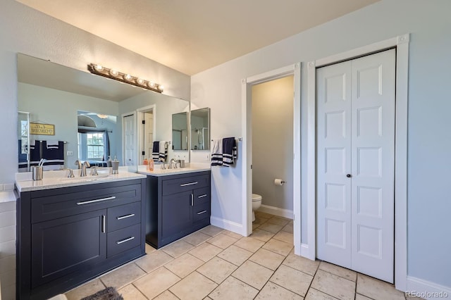 full bath featuring two vanities, a closet, toilet, and a sink