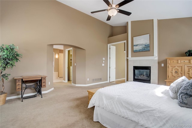 bedroom featuring high vaulted ceiling, a tiled fireplace, light carpet, and ceiling fan