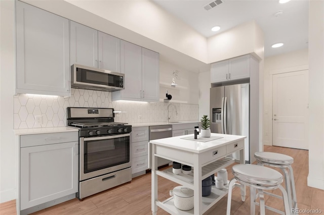 kitchen with appliances with stainless steel finishes, light hardwood / wood-style floors, and backsplash