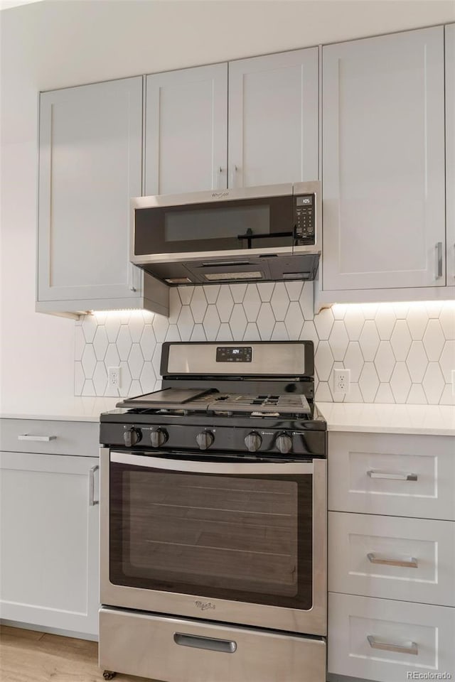 kitchen with light wood-type flooring, appliances with stainless steel finishes, range hood, decorative backsplash, and white cabinets