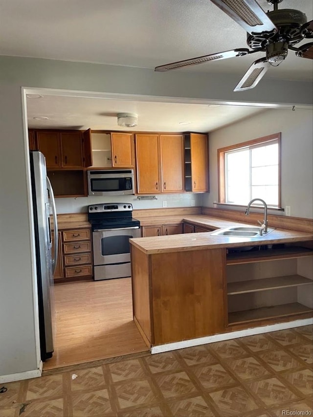 kitchen with a ceiling fan, stainless steel appliances, light countertops, open shelves, and a sink