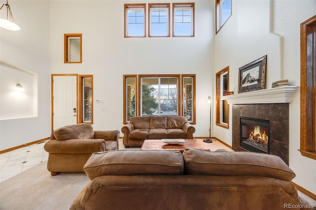 living area with baseboards, a towering ceiling, carpet flooring, and a tile fireplace