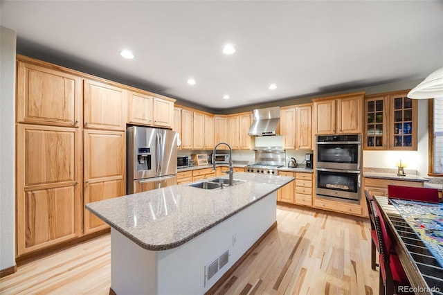 kitchen with light brown cabinetry, appliances with stainless steel finishes, wall chimney range hood, and a sink